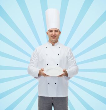 cooking, profession, advertisement and people concept - happy male chef cook showing something on empty plate over blue burst rays background
