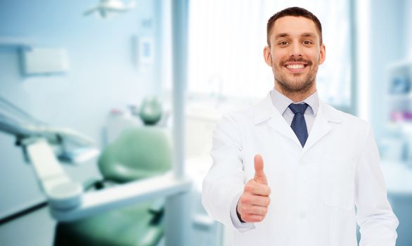 healthcare, profession, stomatology and medicine concept - smiling male dentist showing thumbs up over medical office background