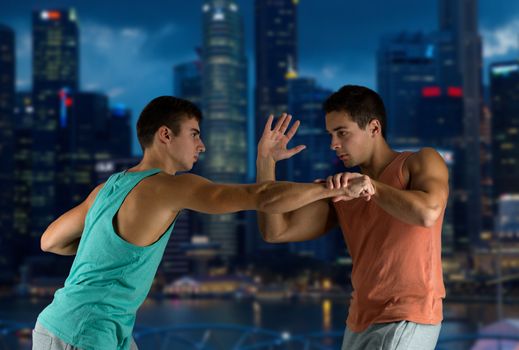 sport, competition, strength and people concept - young men fighting hand-to-hand over night city background