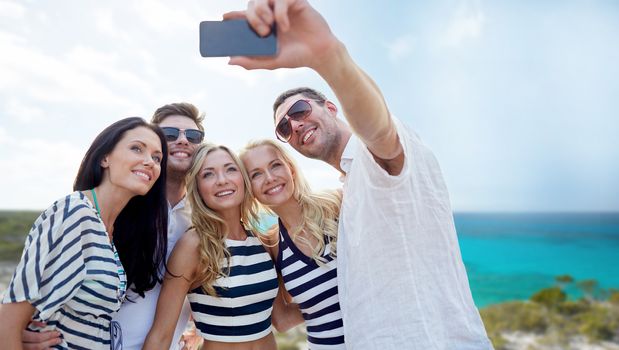summer, sea, tourism, technology and people concept - group of smiling friends with smartphone photographing and taking selfie on beach