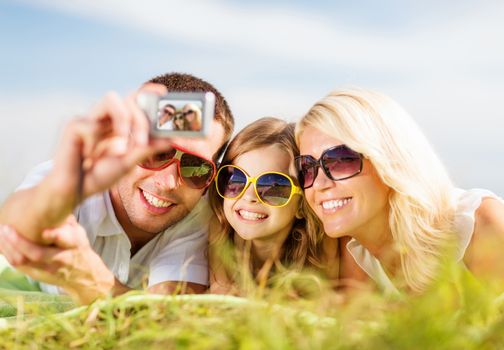 summer holidays, children and people concept - happy family with camera, blue sky and green grass taking picture