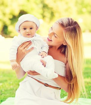 family, child and parenthood concept - happy mother with little baby sitting on blanket in park