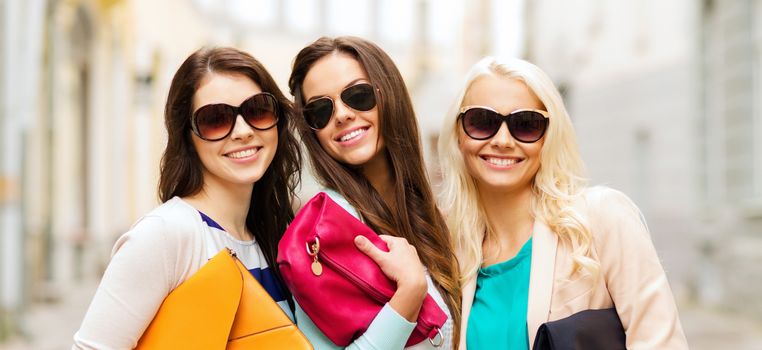 holidays, tourism and happy people concept - three smiling women in sunglasses with bags in the city