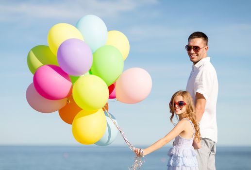 summer holidays, celebration, children and family concept - happy father and daughter with colorful balloons at seaside