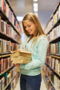 people, knowledge, education and school concept - happy student girl or young woman with book in library