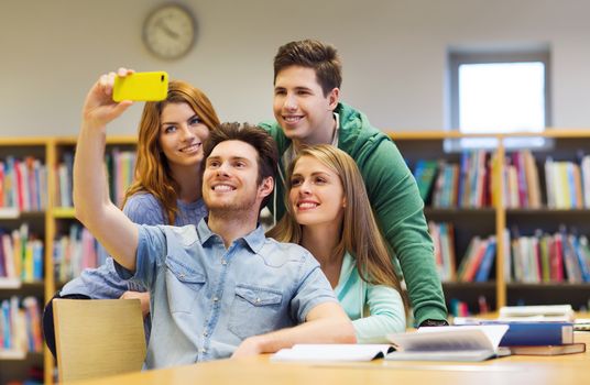 people, technology, education and school concept - happy students or friends with smartphone taking selfie in library