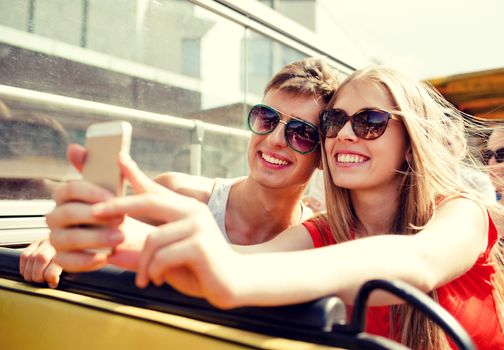 friendship, tourism, summer vacation, technology and people concept - smiling couple with smartphone traveling by tour bus and making selfie