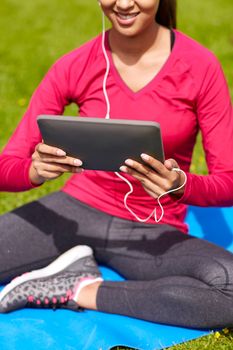 fitness, technology, people and sport concept - close up of smiling african american woman with tablet pc computer sitting on mat outdoors
