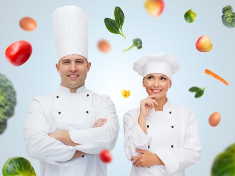 cooking, profession, vegetarian diet and people concept - happy chef couple or cooks over blue background with falling vegetables