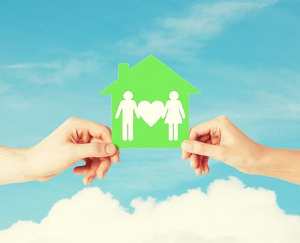 real estate and family home concept - isolated picture of male and female hands holding green paper house with family