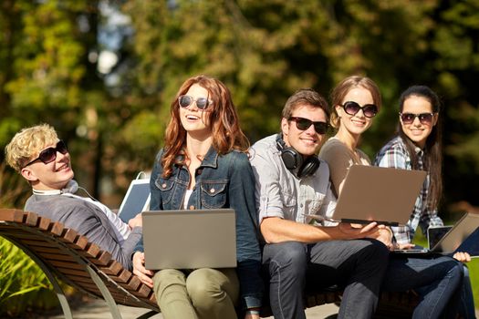 summer, communication, technology , education and teenage concept - group of students or teenagers with laptop and tablet pc computers at park or campus