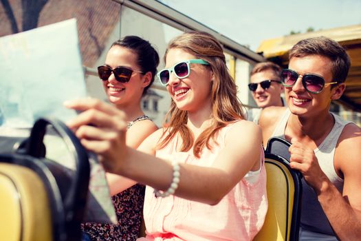 friendship, travel, vacation, summer and people concept - group of smiling friends with map traveling by tour bus