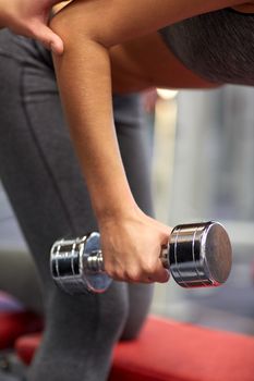 fitness, sport, exercising and weightlifting concept - close up of young woman and personal trainer with dumbbells flexing muscles in gym