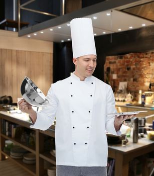 cooking, profession and people concept - happy male chef cook opening cloche cover over kitchen background