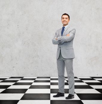 business, people and strategy concept - happy smiling businessman in suit standing on checkerboard pattern floor over gray background