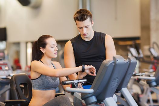 sport, fitness, lifestyle, technology and people concept - woman with trainer working out on exercise bike in gym