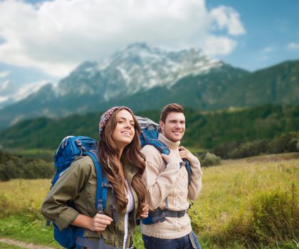 adventure, travel, tourism, hike and people concept - smiling couple walking with backpacks over alpine mountains background