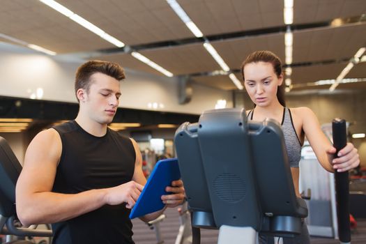 sport, fitness, lifestyle, technology and people concept - woman and trainer with tablet pc computer exercising on stepper in gym