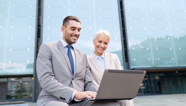 business, education, technology and people concept - smiling businesspeople working with laptop computer on city street