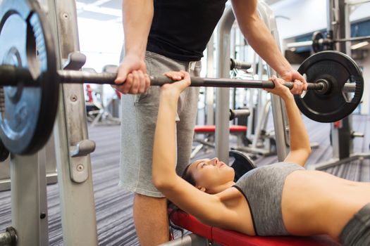 sport, fitness, teamwork, weightlifting and people concept - young woman and personal trainer with barbell flexing muscles in gym