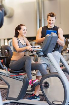 sport, fitness, lifestyle, technology and people concept - happy woman with trainer working out on exercise bike in gym