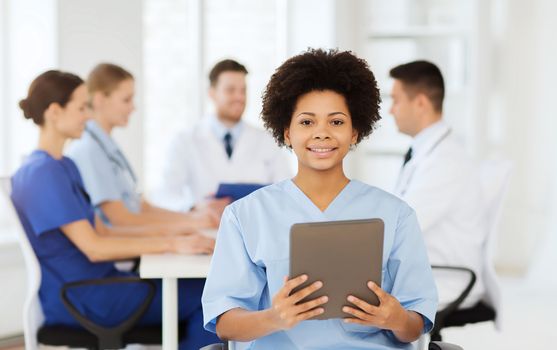 clinic, profession, people and medicine concept - happy female doctor or nurse with tablet pc computer over group of medics meeting at hospital