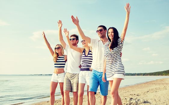 summer, holidays, sea, tourism and people concept - group of smiling friends in sunglasses walking on beach and waving hands