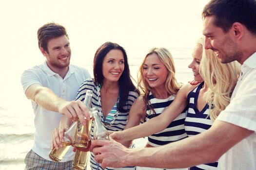 summer, holidays, tourism, drinks and people concept - group of smiling friends clinking bottles of beer or cider on beach