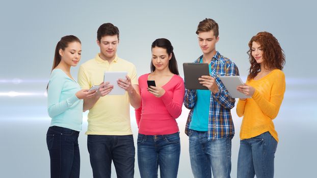 friendship, technology and people concept - group of smiling teenagers with smartphones and tablet pc computers over gray background with laser light