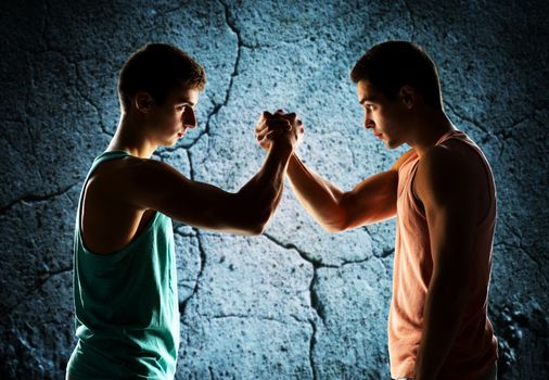 sport, competition, strength and people concept - two young men arm wrestling over concrete wall background
