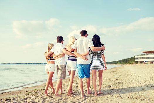 summer, holidays, sea, tourism and people concept - group of smiling friends hugging and walking on beach from back