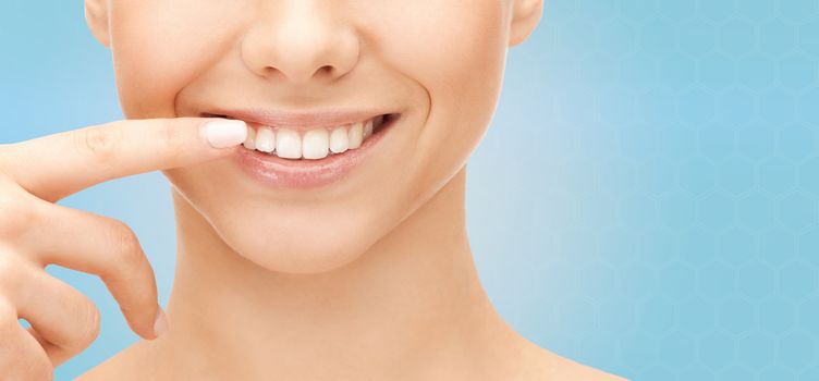 dental health, beauty, hygiene and people concept - close up of smiling woman face pointing to teeth over blue background