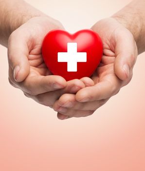 family health, charity and medicine concept - close up of male hands holding red heart with white cross over beige background
