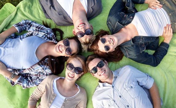summer holidays, friendship, leisure and teenage concept - group of students or teenagers lying in circle at campus or park