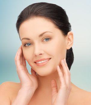 beauty, people and health concept - beautiful young woman touching her face over blue background