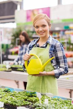 people, gardening and profession concept - happy woman or gardener with watering can and seedling in greenhouse