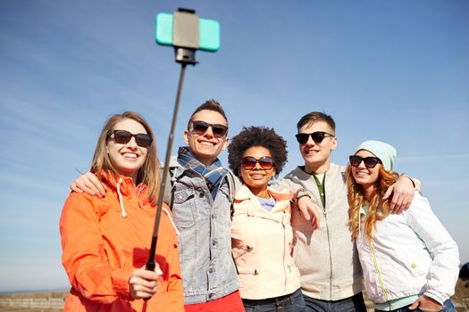 tourism, travel, people, leisure and technology concept - group of smiling teenage friends taking selfie with smartphone and monopod on city street