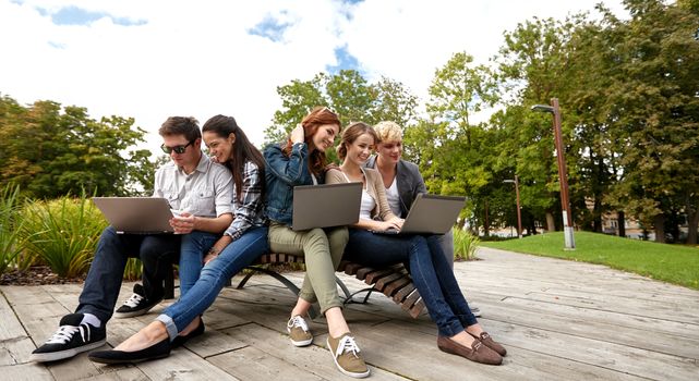 summer, communication, technology , education and teenage concept - group of students or teenagers with laptop computers at park or campus