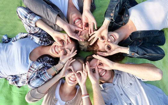 summer holidays, friendship, leisure and teenage concept - group of students or teenagers lying in circle and having fun at campus or park