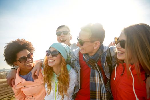 tourism, travel, people, leisure and teenage concept - group of happy friends in sunglasses hugging and laughing on city street