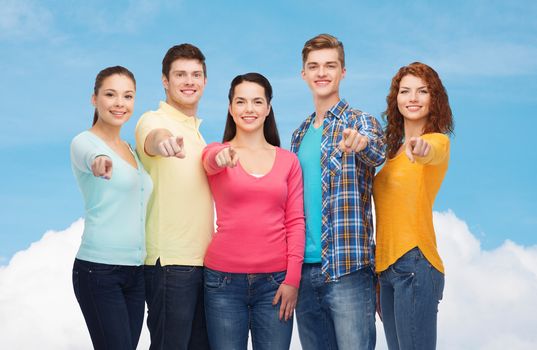 friendship, dream, future and people concept - group of smiling teenagers pointing fingers on you over blue sky with white cloud background