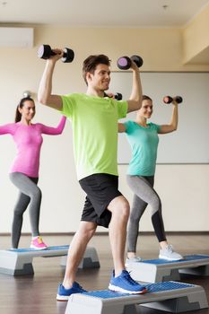 fitness, sport, aerobics and people concept - group of smiling people working out with dumbbells flexing muscles on step platforms in gym
