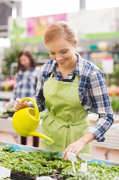 people, gardening and profession concept - happy woman or gardener with watering can and seedling in greenhouse