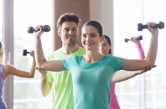 fitness, sport, training, gym and lifestyle concept - group of happy women and trainer with dumbbells flexing muscles in gym