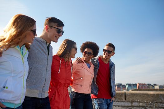 tourism, travel, people and leisure concept - group of happy teenage friends walking along city street and talking