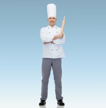 cooking, profession and people concept - happy male chef cook holding rolling pin over blue background