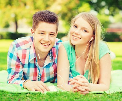 vacation, holidays, technology and friendship concept - smiling couple with smartphone and earphones lying on blanket in park