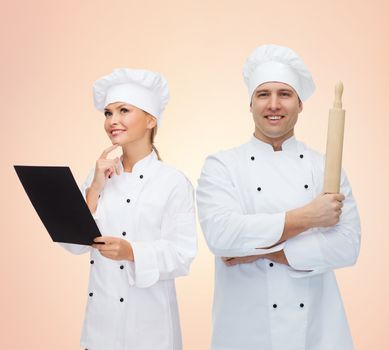 cooking, baking, teamwork, profession and people concept - happy chefs or cooks couple with menu and rolling pin over beige background
