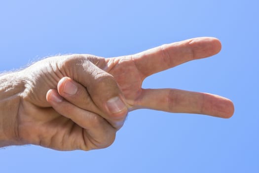 Closeup low angle of male hand showing peace sign with blue sky background on sunny day in natural light