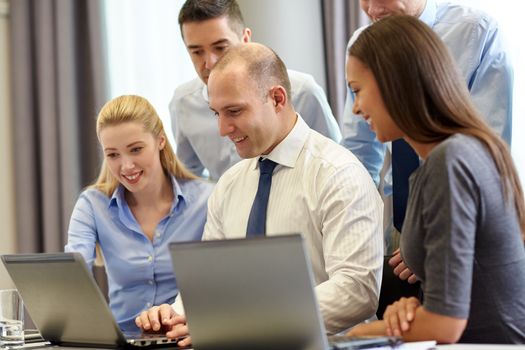 business, people and technology concept - smiling business team with laptop computers meeting in office